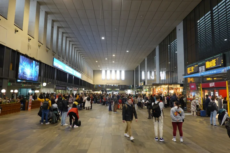 Viajeros en el vestíbulo de Sevilla Santa Justa, con paneles informativos junto a los comercios